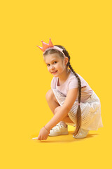 Little girl in crown drawing with chalk piece on yellow background. Children's Day celebration