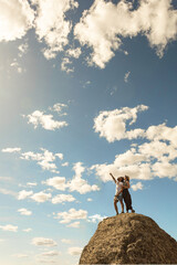 couple taking selfie in nature, pointing to the sky on rocks and white clouds in sky, summer time vertical photography