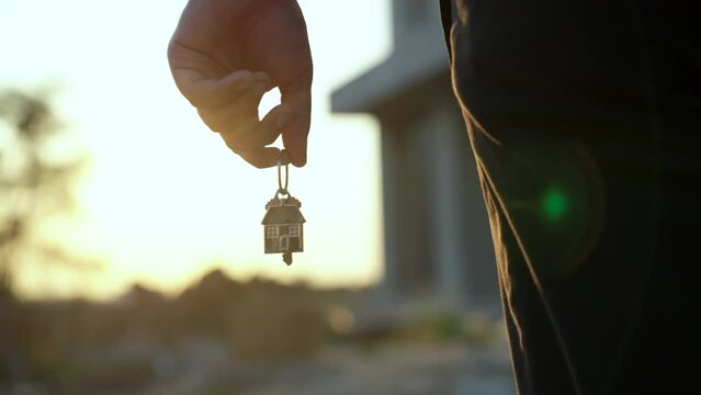 
Close-up key in hand of landlord a new house on the background of a beautiful sunset. Slow motion hand holding key a new home. Real estate concept.

