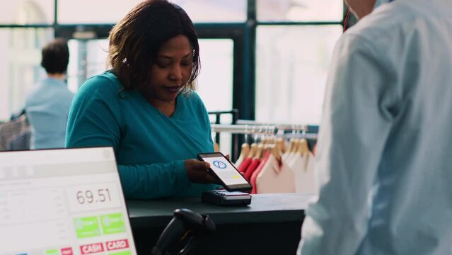 African american client paying for casual wear with mobile phone nfc on pos terminal, buying fashionable clothes and accessories in modern boutique. Woman standing at retail store Generative AI