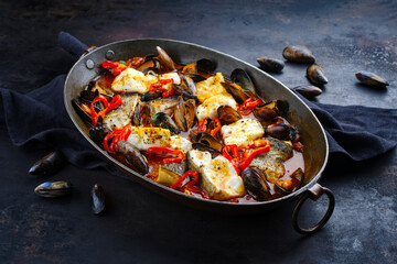 Traditional French seafood bouillabaisse with cod fish and mussels in red wine tomato sauce served as close-up in a rustic copper casserole