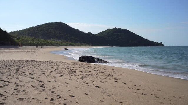 Footprints on sand of tropical beach with waving sea. Praia do Buraco beach with Morro do Careca hills in Balneario Camboriu, Santa Catarina, Brazil.