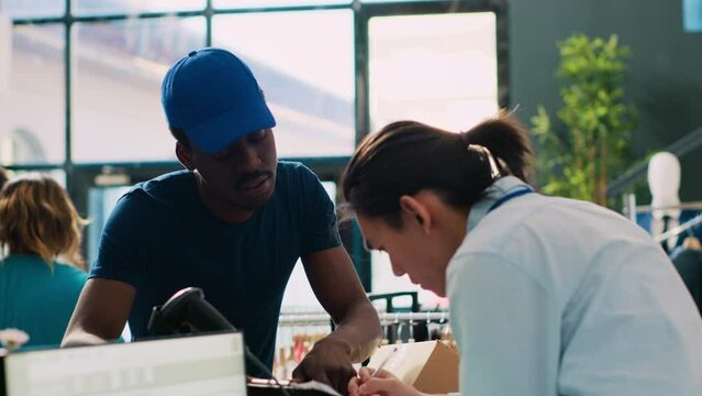 Asian worker signing packages delivery report, discussing clothes distribution with african american courier in modern boutique. Store manager preparing boxes with customers orders in Generative AI