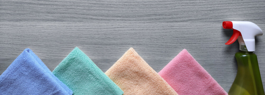 Banner with spray and window cleaning rags. Multicolored synthetic rags and household chemicals spray on wooden background. Header for website, advertisement, cleaning company blog, hardware store