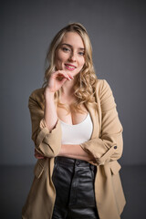 Hübsche blonde Frau in beigen Mandel mit weißem Oberteil und schwarzem Minirock lächelt