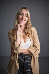 Hübsche blonde Frau in beigen Mandel mit weißem Oberteil und schwarzem Minirock lächelt