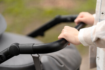 Fototapeta na wymiar Closeup, selective focus, woman holding stroller with her hands. ?aring mother walking outdoors