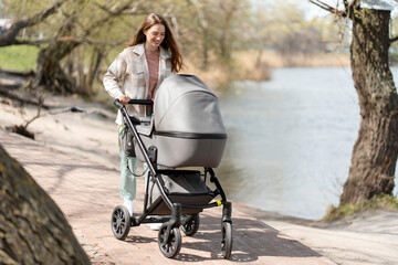 Modern, young mother walking pushing stroller with baby outdoors, walking in park. Happy woman