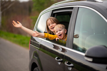 Happy brother and sister looking out car window , rejoice and laugh