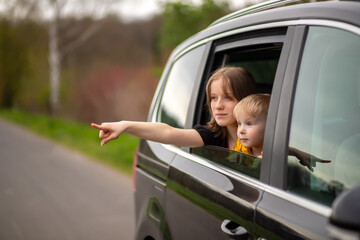 Happy brother and sister looking out car window , point the finger to the side and look in surprise
