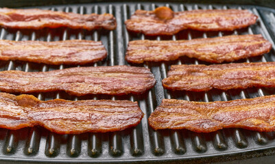 Crispy hot fried bacon pieces on a grill, selective focus. grilled bacon close up.