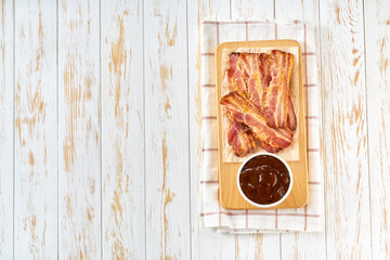 fried bacon strips and bbq sauce on a table, top view.