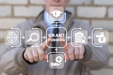 Businessman using virtual touch screen presses inscription: GRANT FUNDING. Concept of grants and...