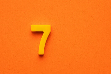 Number seven yellow plastic - plastic digit on orange foamy background