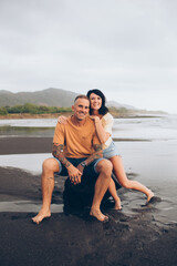 couple sitting on a rock smiling at the camera at the beach