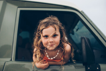 young girl with curly hair leaning out of a car