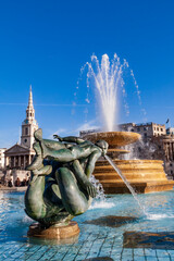 Trafalgar Square fountain and the Royal Gallery Museum building in London under a blue summer sky.
