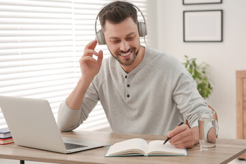 Online translation course. Man in headphones writing near laptop at home