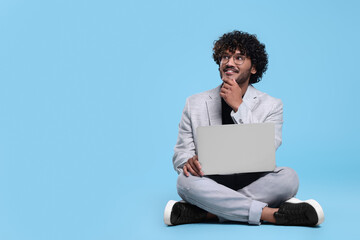 Smiling man with laptop on light blue background, space for text