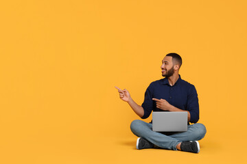Smiling young man with laptop on yellow background, space for text