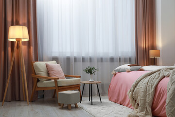 Stylish bedroom with comfortable bed, armchair and wooden table. Interior design