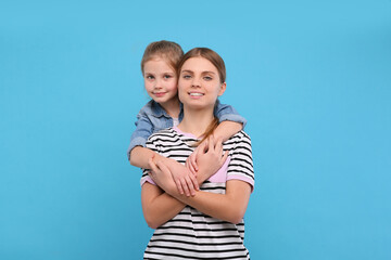 Fototapeta na wymiar Little daughter hugging her mom on light blue background. Happy Mother's Day