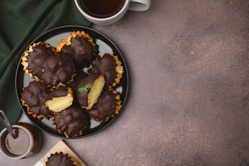 Delicious profiteroles with chocolate spread, cream and aromatic tea on textured table, flat lay. Space for text