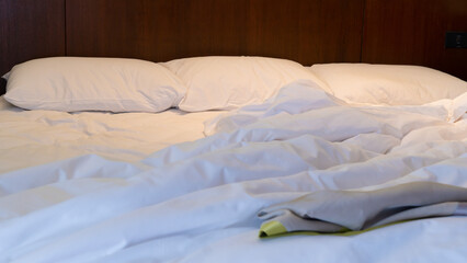 White mattress with blankets scattered. Three pillows lined up. Warm light in the bedroom.