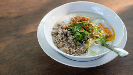 Minced Pork Congee with Egg on white bowl. Spoons are placed and plates are supported on a wooden table top.