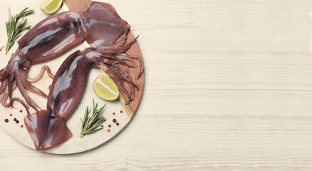 Board with fresh squids, slices of lime and rosemary on wooden table, flat lay. Banner design with space for text