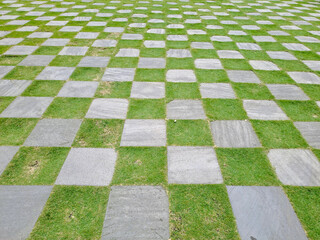 Pattern of square cement floor tiles with green . walkway with green grass in the park. Stone pathway and green grass at park. Garden Stepping Stone Path through Green Grass Law.