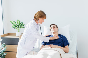 the doctor is examining the patient in the hospital. Caucasian female doctor talking to male patient lying in hospital bed.