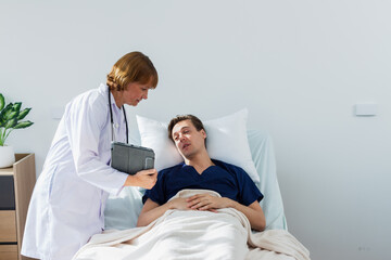 the doctor is examining the patient in the hospital. Caucasian female doctor talking to male patient lying in hospital bed.