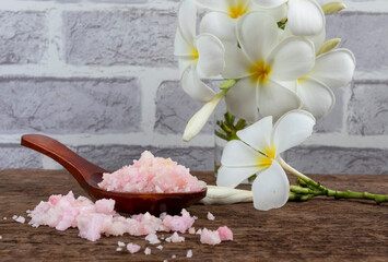 Pink sea salt on a wooden background with frangipani flower. Spa concept healthy and relax