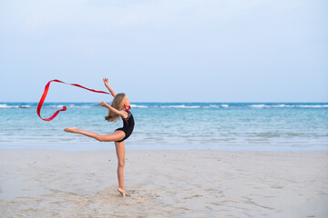 girl gymnast makes an element with a ribbon on the beach, rhythmic gymnastics