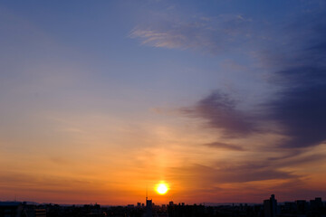 都市の夜明け。日の出とともに空と雲がオレンジ色に染まり、ビル群はシルエットとして写す