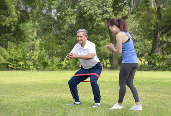 young woman trainer teaching a senior man doing exercise with elastic band,smiling woman applauding beside him,legs stretch exercise for rehabilitation muscles in older adult,concept of elderly health