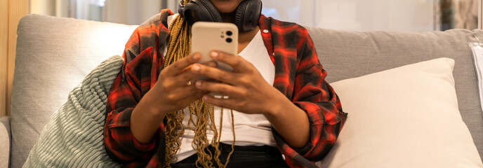 Portrait of of smiling happy african woman relaxing use technology of smartphone at home.Young african creative girl looking at screen typing message and playing game online or social media