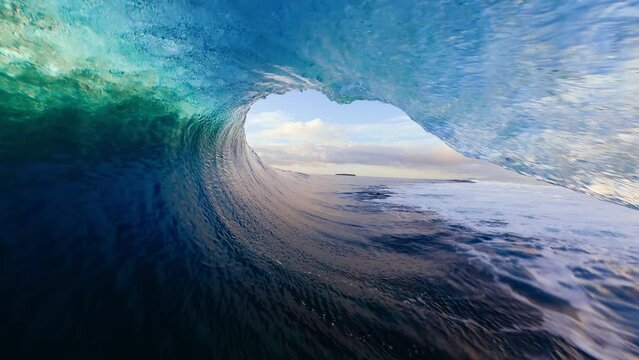 View from inside the tube of surfer riding perfect ocean wave at sunset, POV of surfer in the barrel