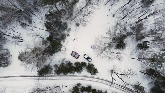 Aerial descending top down view of camp tent and white truck in snow forest