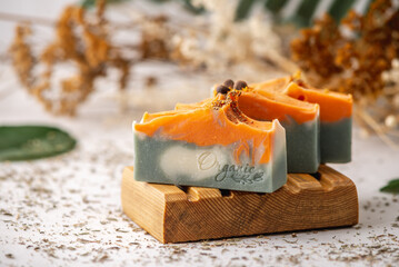 Pieces of bright natural handmade soap on a wooden soap dish with green leaves around