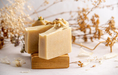 Delicate natural beige handmade soap in a wooden soap dish on a white background with flowers and petals.