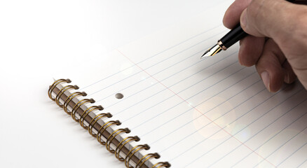 A man's hand holding a fountain pen riting down on notepad