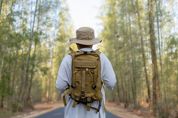 Naklejka premium Young Asian man with a backpack and hat hiking in the mountains during the summer season, a traveler walking in the forest. Travel, adventure, and journey concept.