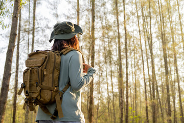 Young Asian girl with a backpack and hat hiking in the mountains during the summer season, a traveler walking in the forest. Travel, adventure, and journey concept.