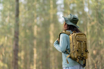 Naklejka premium Young Asian girl with a backpack and hat hiking in the mountains during the summer season, a traveler walking in the forest. Travel, adventure, and journey concept.