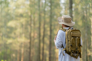 Young Asian man with a backpack and hat hiking in the mountains during the summer season, a...