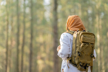 Muslim Asian woman wearing hijab with a backpack and hat hiking in the mountains during the summer season, a traveler walking in the forest. Travel, adventure, and journey concept.