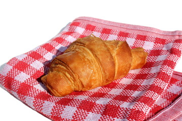 A fresh baked croissant lies on a red checkered napkin.