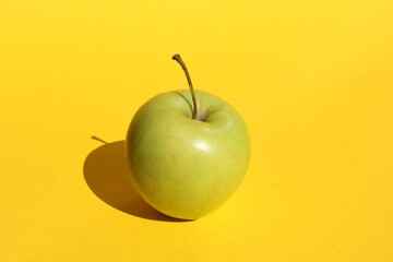 A green juicy apple lies on a yellow background with sharp shadow